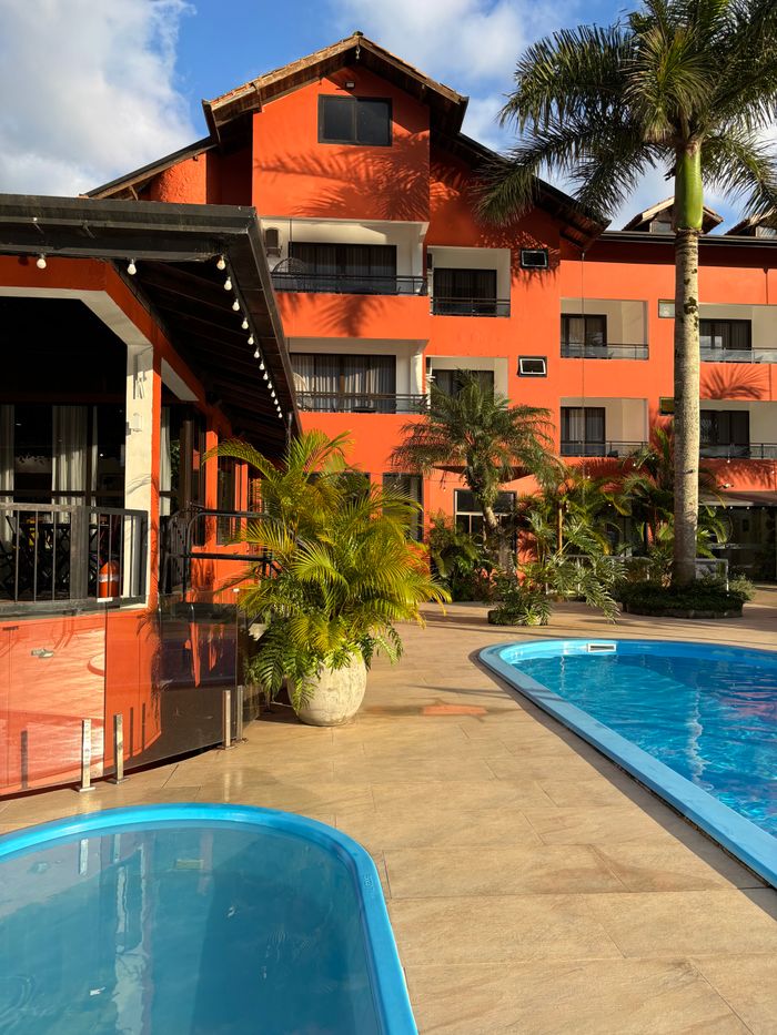 Bright orange hotel surrounded by lush greenery and pools, offering a tropical escape.